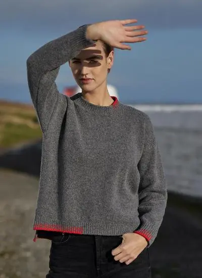 woman standing by the sea wearing grey sweater blocking sun from her face